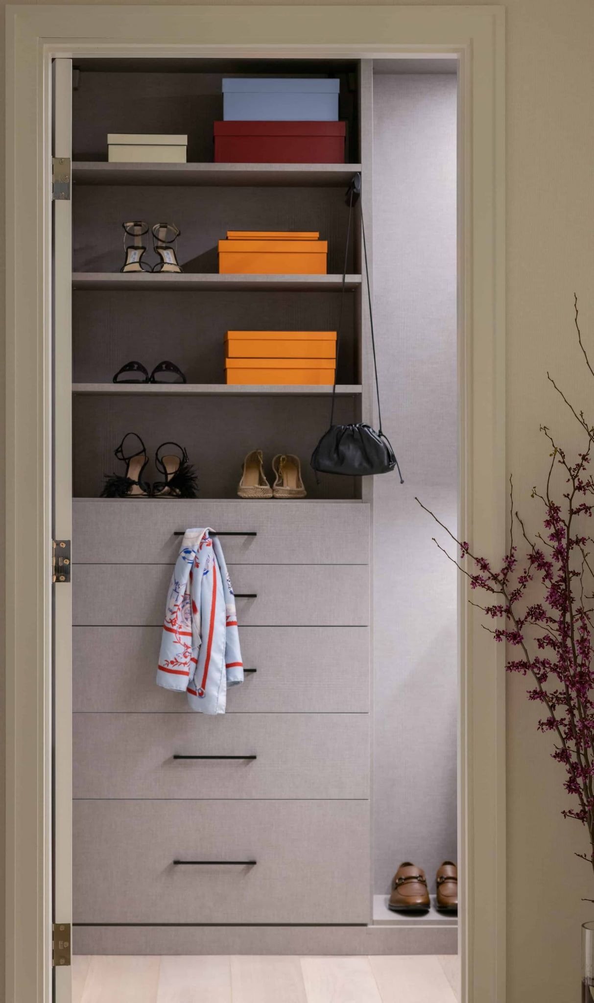 Walk-in closet with gray built-ins, displayed shoes and handbags, colorful boxes, and a patterned scarf.