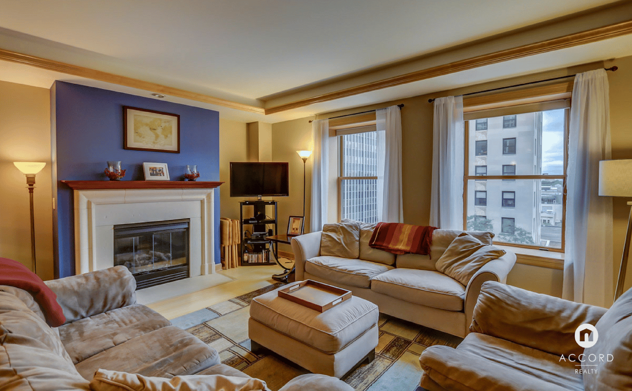 Condo living room with a fireplace, cream sofas, large windows, and a purple accent wall.