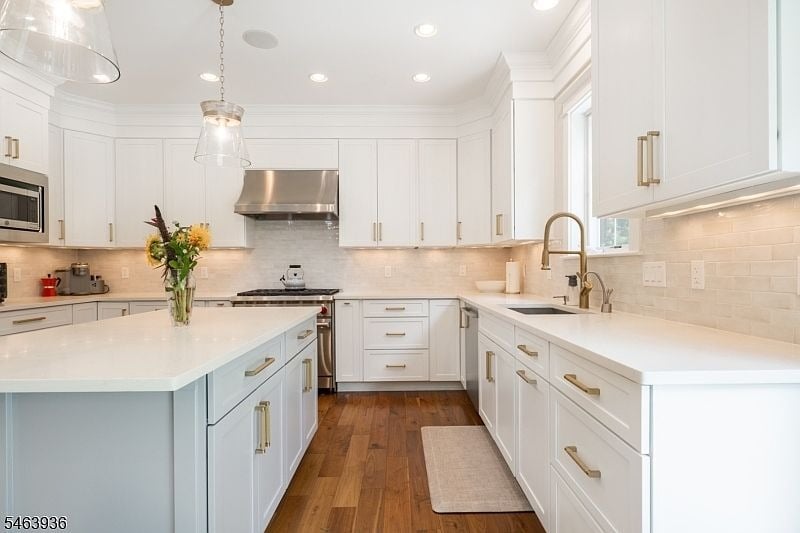 White kitchen with a large island, brass hardware, pendant lights, and warm wood floors.