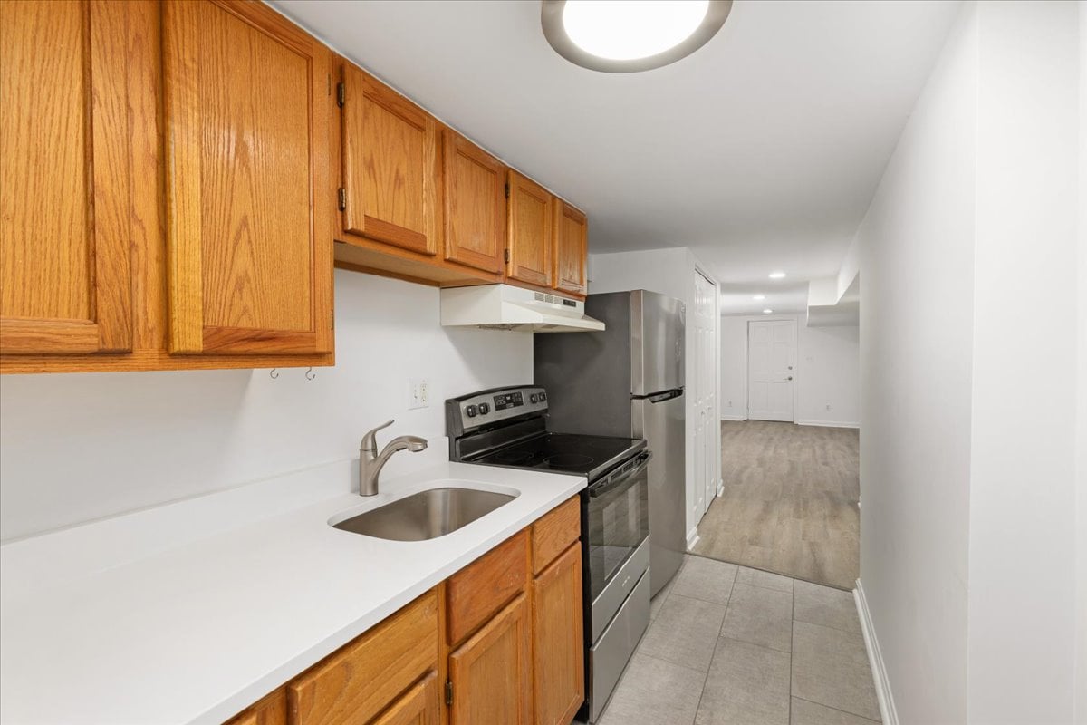Galley kitchen with wood cabinets, white counters, and stainless-steel appliances.