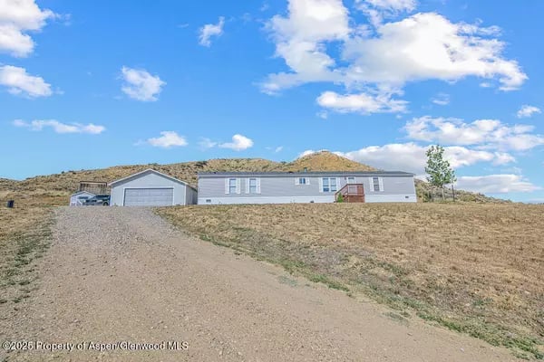 Single-story home with an attached garage at the top of a gravel driveway on a dry hillside.