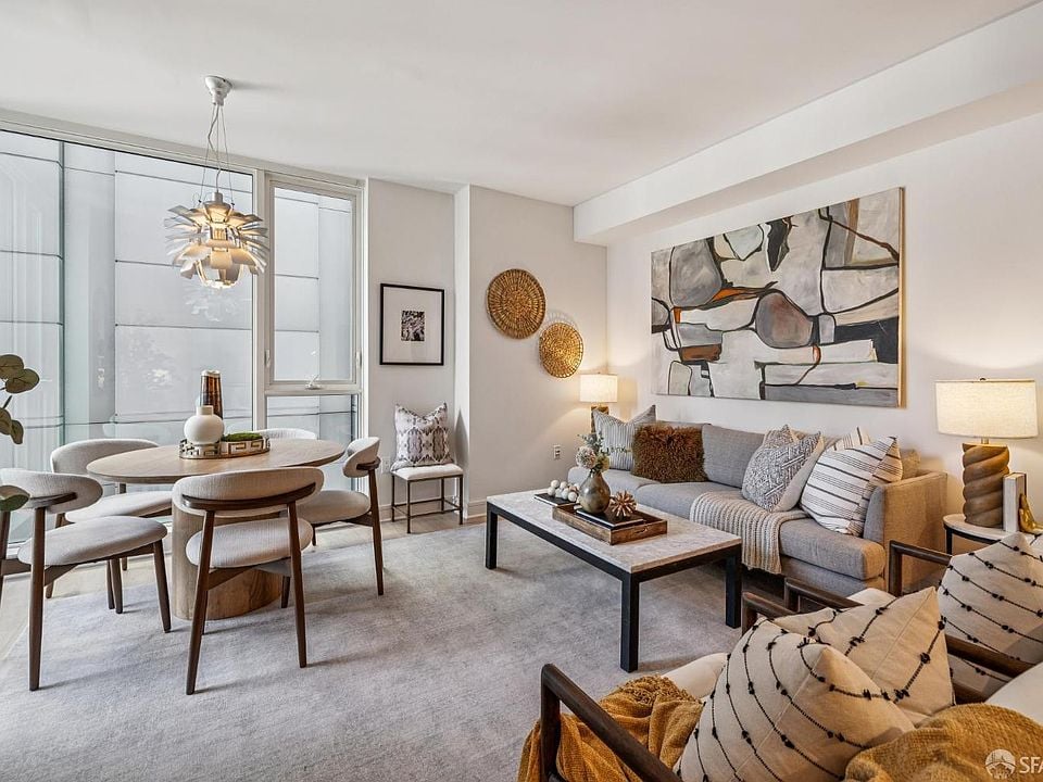 Staged open-plan living and dining room with a gray sofa, abstract art, and large windows.