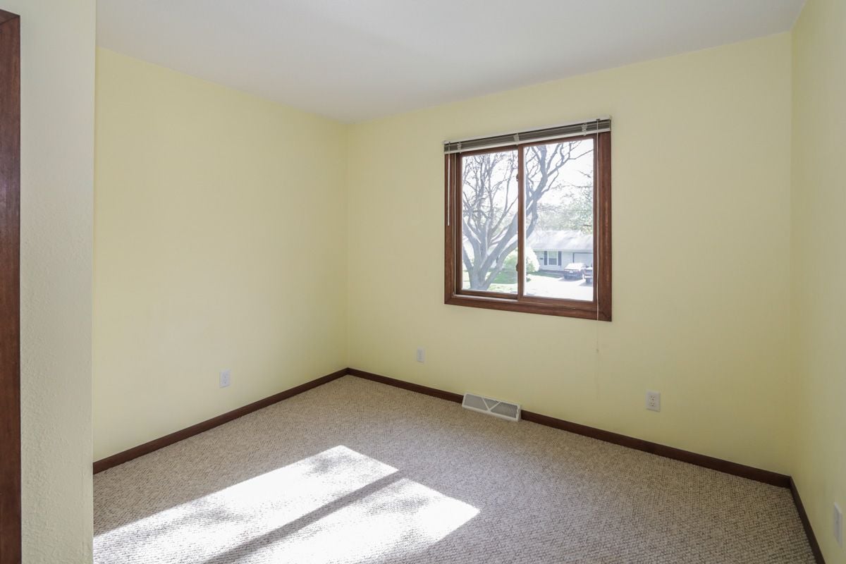 Empty carpeted room with pale yellow walls, dark wood trim, and sunlight through a window.