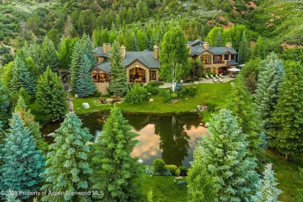 Aerial view of a mountain home surrounded by trees, with a pond and landscaped grounds.