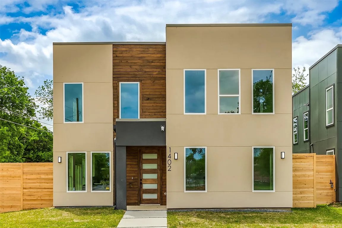 Modern two-story home with wood accents, tall windows, and a fenced front yard.