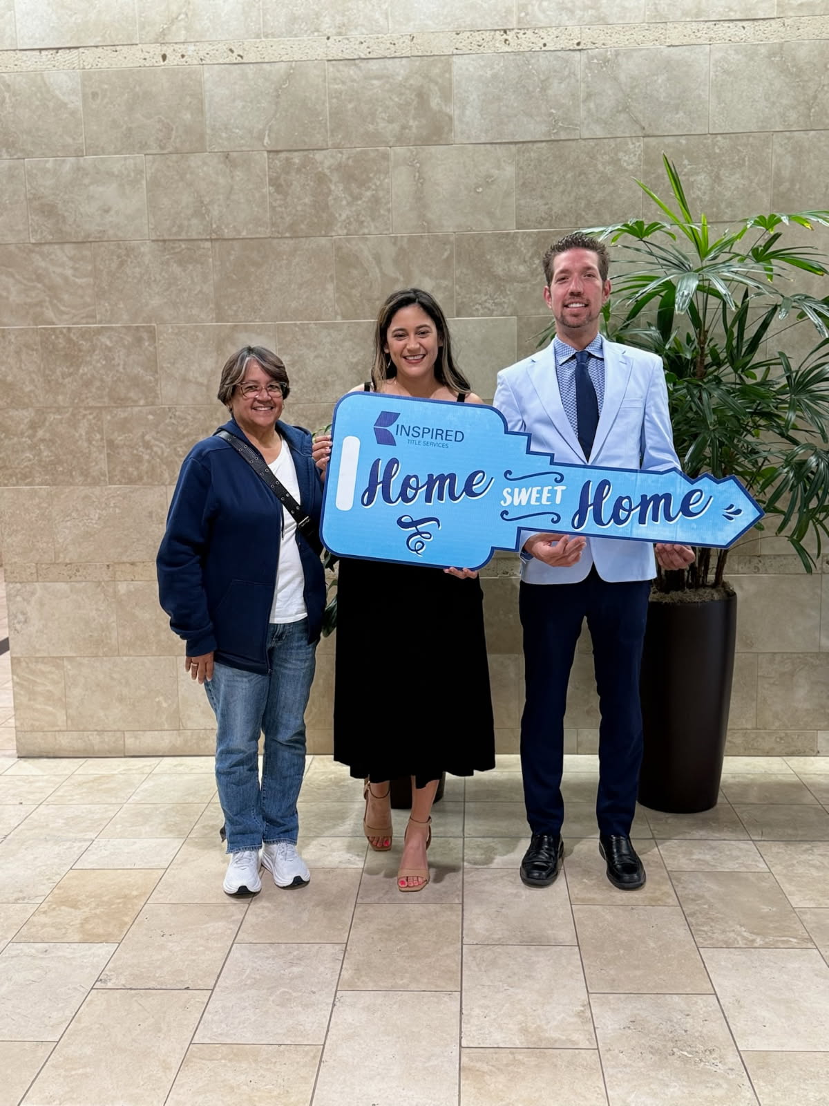Three adults pose with a blue “Home Sweet Home” sign from Inspired Title Services.