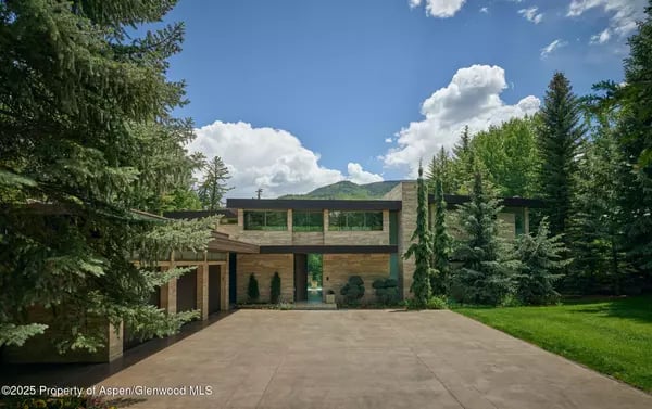 Modern two-story home with a stone and timber facade, broad driveway, and mountain backdrop.