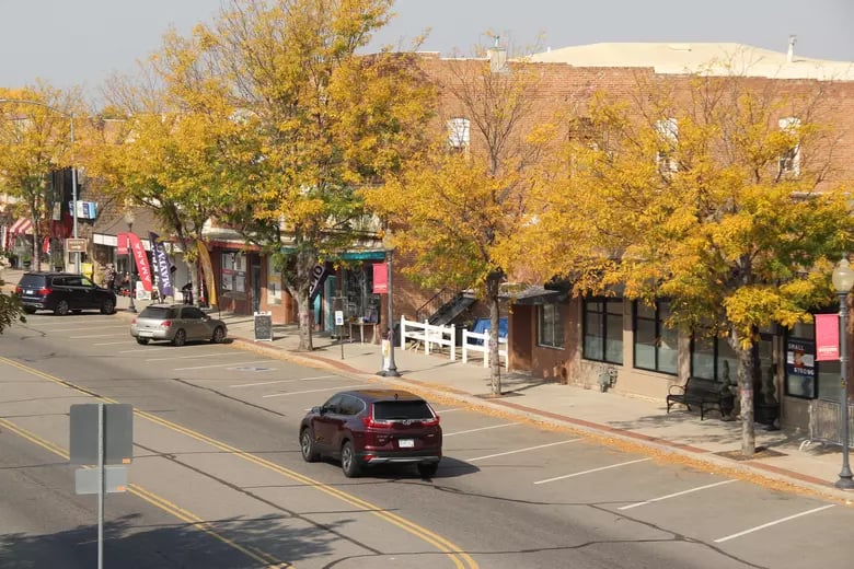 Downtown street with brick storefronts and golden autumn trees.