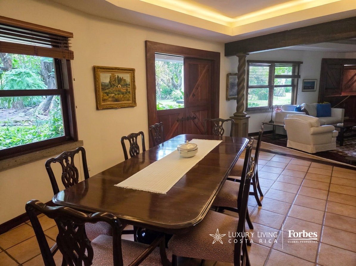 Dining room with a long dark wood table, carved chairs, and garden views through timber-framed windows.