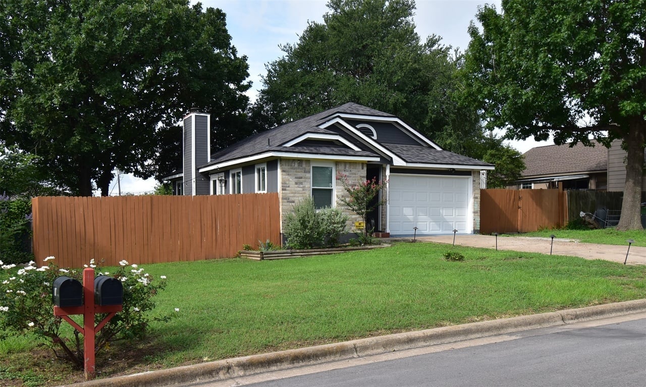 Single-story gray house with stone accents, a white garage door, and a tall wooden fence.