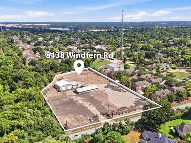 Aerial view of a cleared parcel outlined in white, with small structures amid a leafy residential neighborhood.