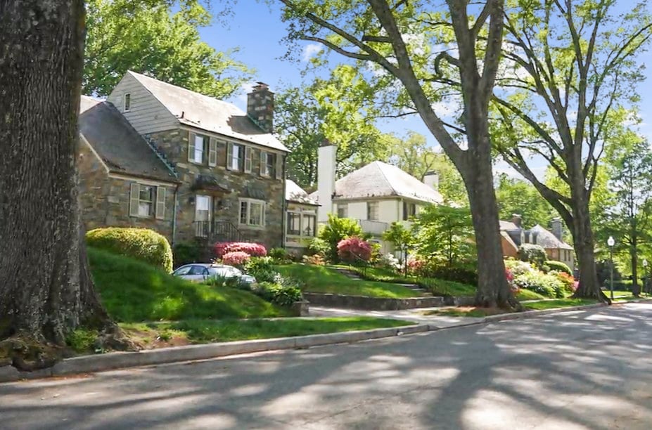 Stone house and neighboring homes along a leafy residential street.