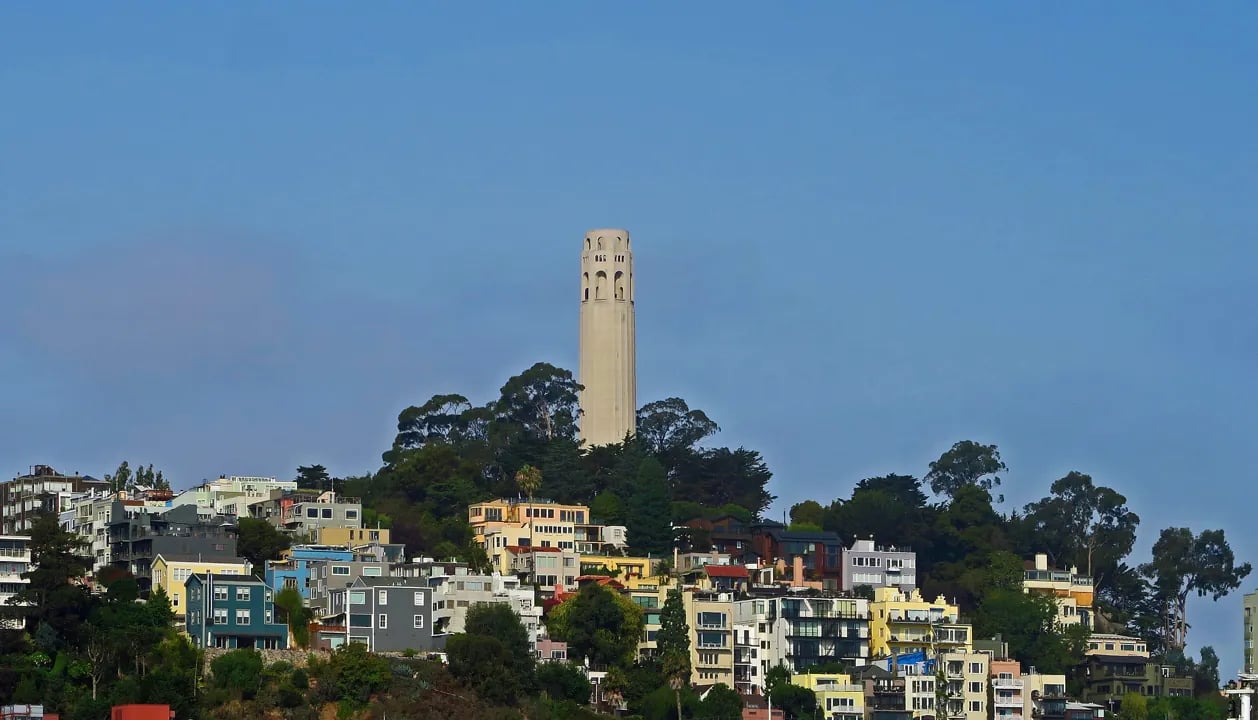Coit Tower rising above colorful Telegraph Hill houses in San Francisco with clear blue sky