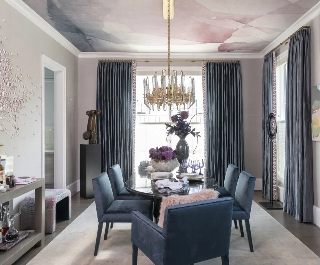 Dining room with an abstract painted ceiling, crystal chandelier, and blue velvet chairs.