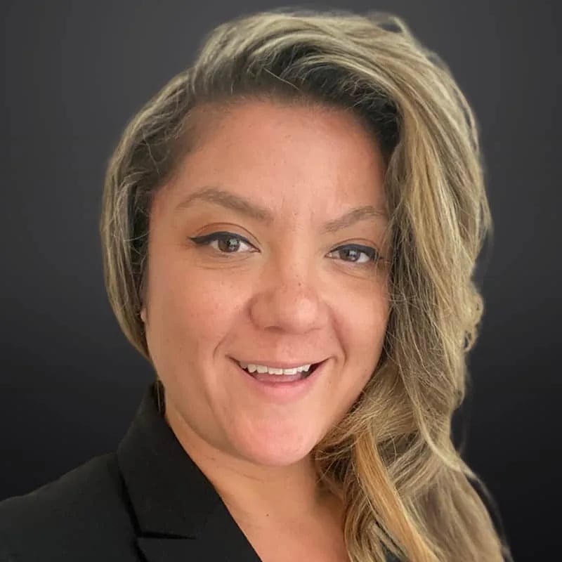 Yelena Pesic smiling in a black jacket, with highlighted hair swept to one side.