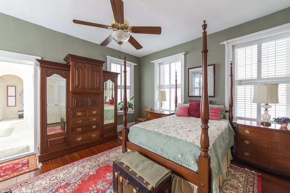 Bedroom with a dark wood canopy bed, antique mirrored armoire, and floral quilt.