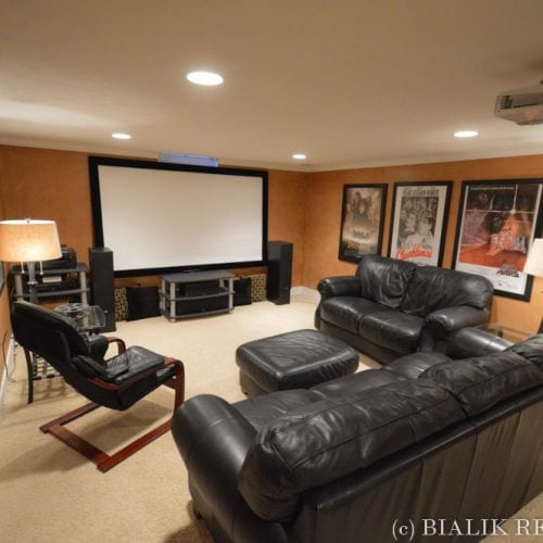 Home theater with a projection screen, black leather seating, surround speakers, and framed movie posters.