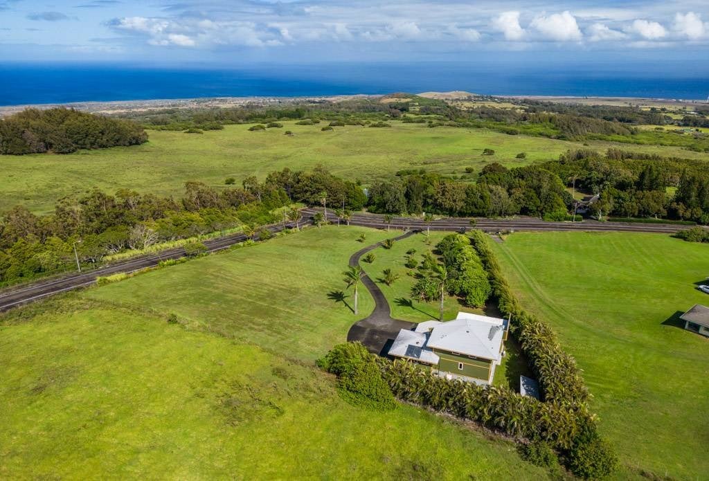 Aerial view of a coastal property amid open green fields, with ocean on the horizon.
