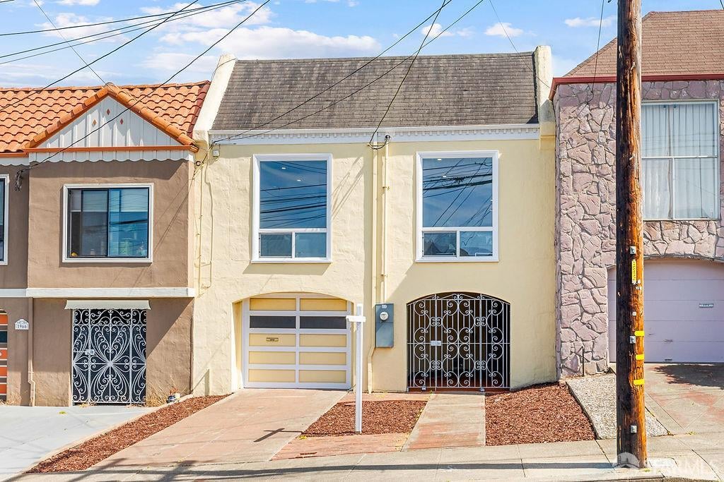 Pale yellow narrow home with an ornate black metal entry gate and garage door.