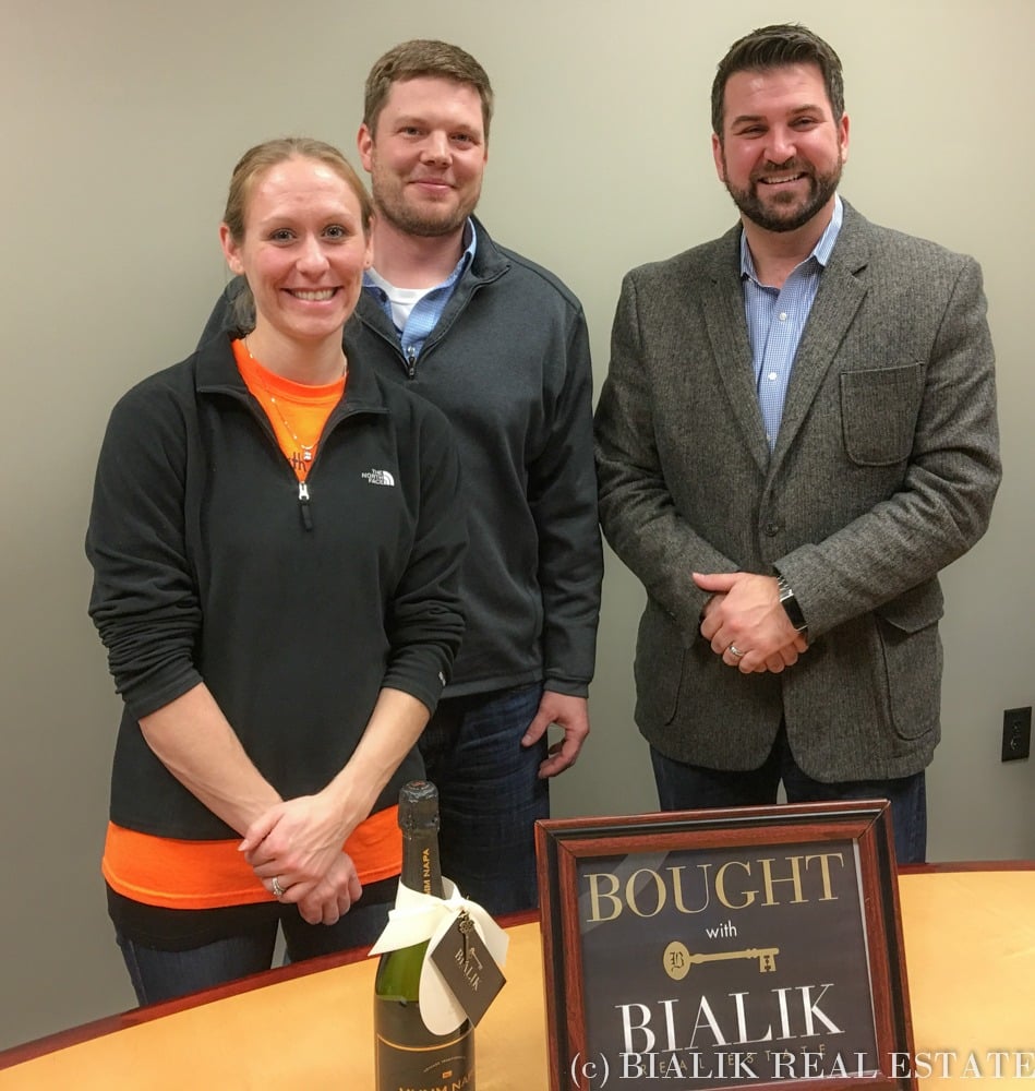 Three adults celebrate a home closing beside a champagne bottle and “Bought with Bialik” sign.