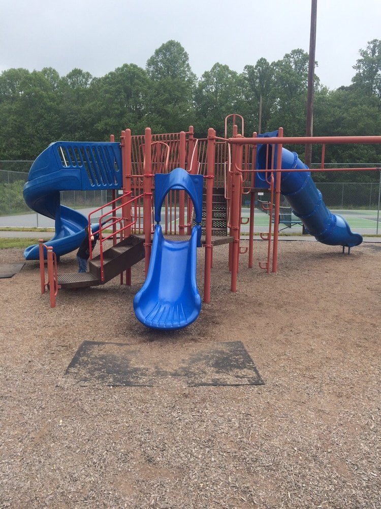 Playground with red climbing structures and several blue slides on a wood-chip surface.