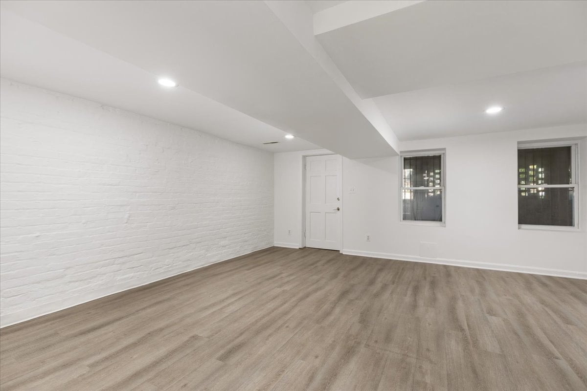 Empty room with a white brick wall, two windows, and wood-look flooring.