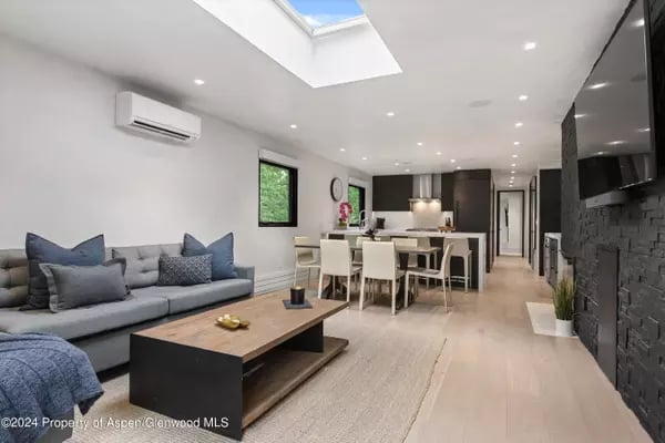 Open-plan living room with gray sectional, dining area, kitchen, and large skylight.