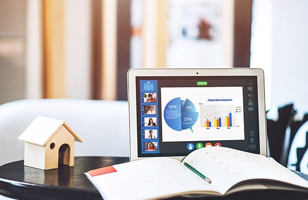 Model house beside an open notebook and pen, with financial charts on a laptop.