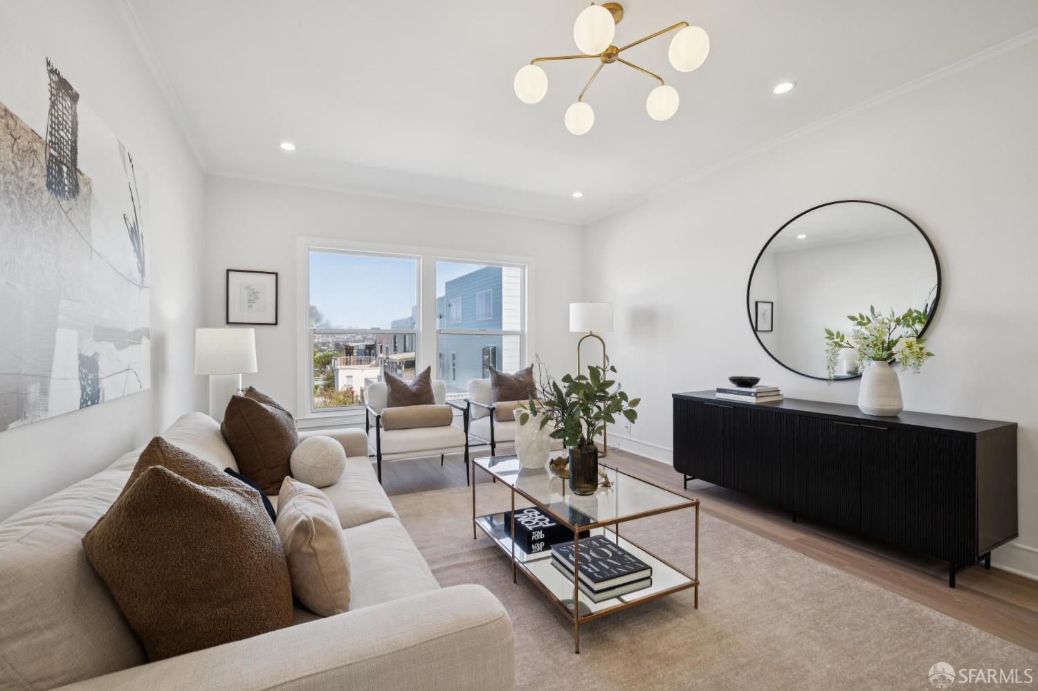 Staged living room with a cream sofa, glass coffee table, and large windows overlooking neighboring buildings.