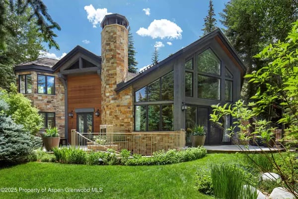 Modern mountain home with a stone chimney, timber siding, and expansive gabled windows.