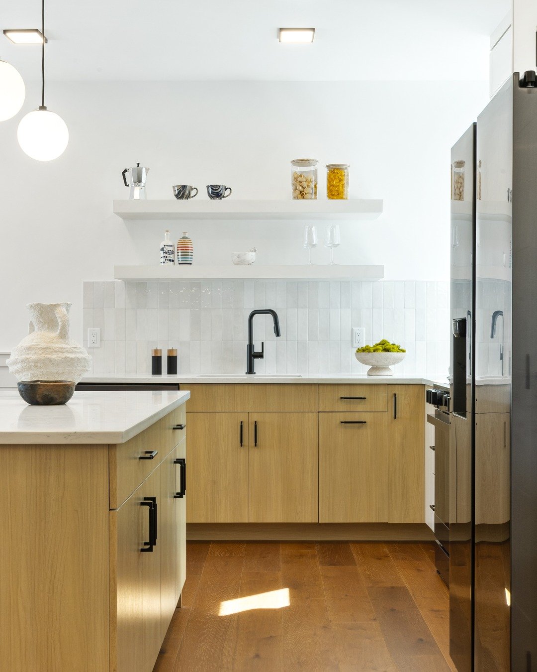 Modern condo kitchen with light oak cabinets, floating shelves, and stainless steel appliances.