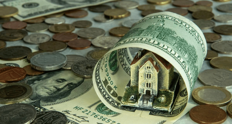 A miniature house surrounded by dollar bills and coins.