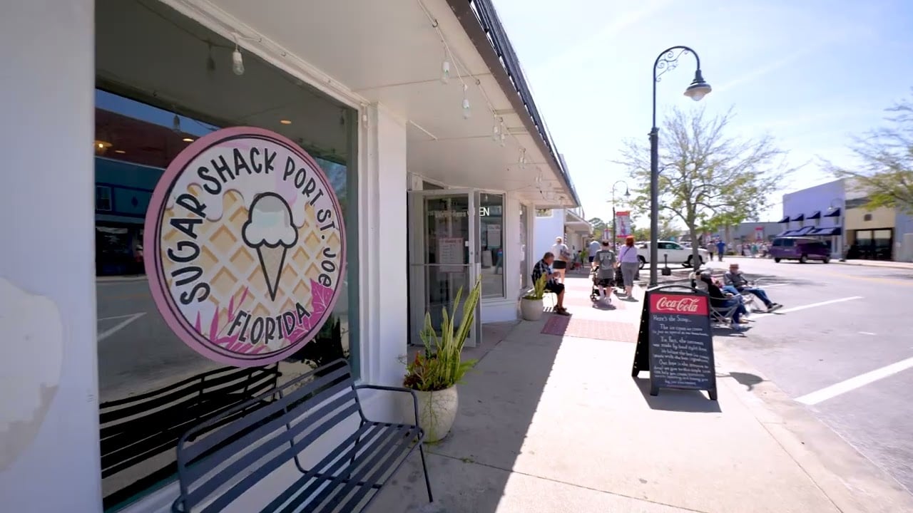 Port St. Joe sidewalk with the Sugar Shack storefront, bench, and pedestrians.