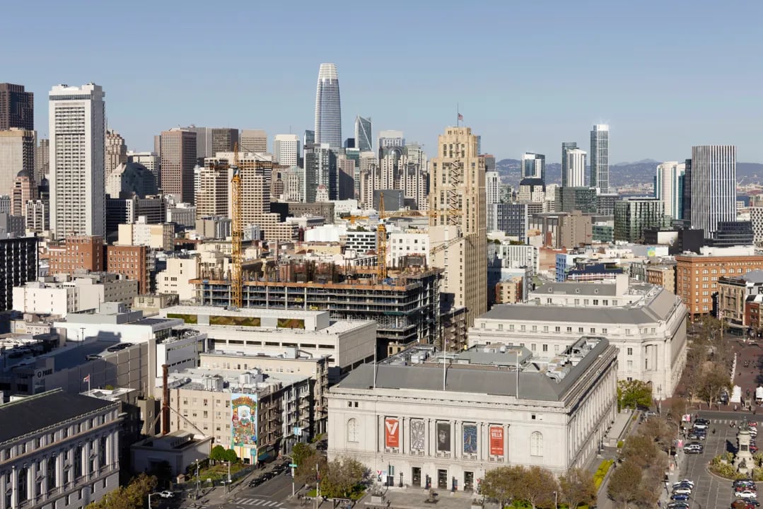 Aerial view of the San Francisco Civic Center featuring the Asian Art Museum in the foreground and the downtown skyline behind it.