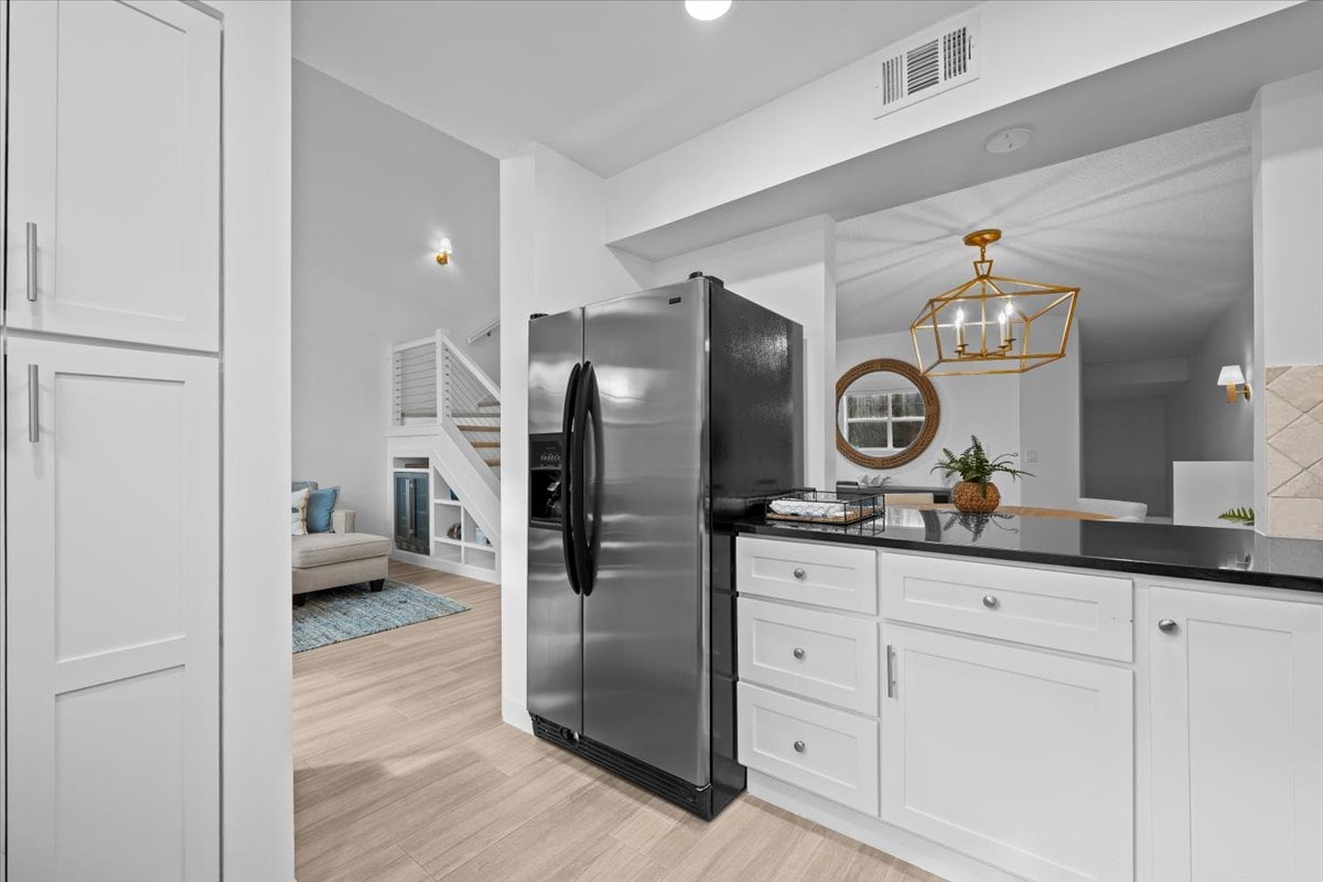 Condominium kitchen with white cabinets, a stainless-steel refrigerator, and an open living area beyond.