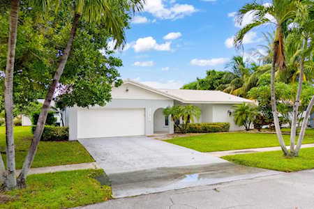 Single-story white home with a two-car garage, broad driveway, and tropical landscaping.