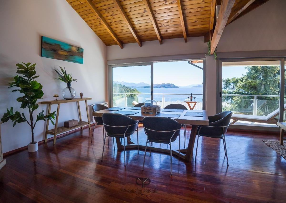 Furnished dining room with a timber ceiling and broad windows overlooking a lake and mountains.