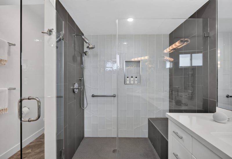 Modern bathroom with a glass-enclosed walk-in shower, tiled walls, built-in niche, and white vanity.