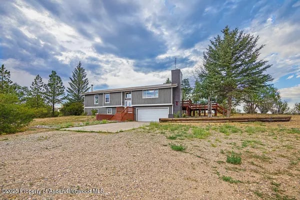 Split-level gray home with an attached garage and raised wooden deck in a broad open yard.