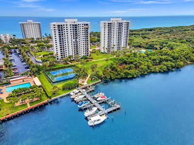 Waterfront condominium towers beside a marina, with boats docked along the blue water.