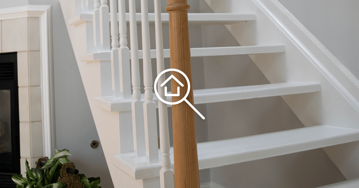 White staircase with a wooden newel post, beside a fireplace.