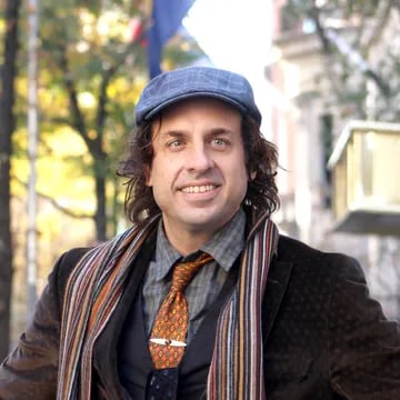 Brennan Stultz wearing a blue flat cap, patterned tie, and striped scarf outdoors.