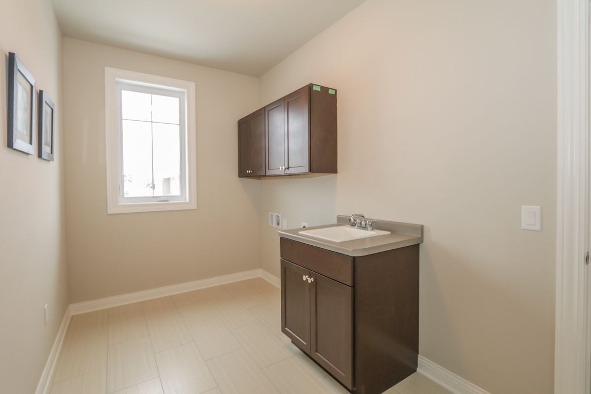 Vacant tiled utility room with a dark wood sink vanity, wall cabinets, and a window.