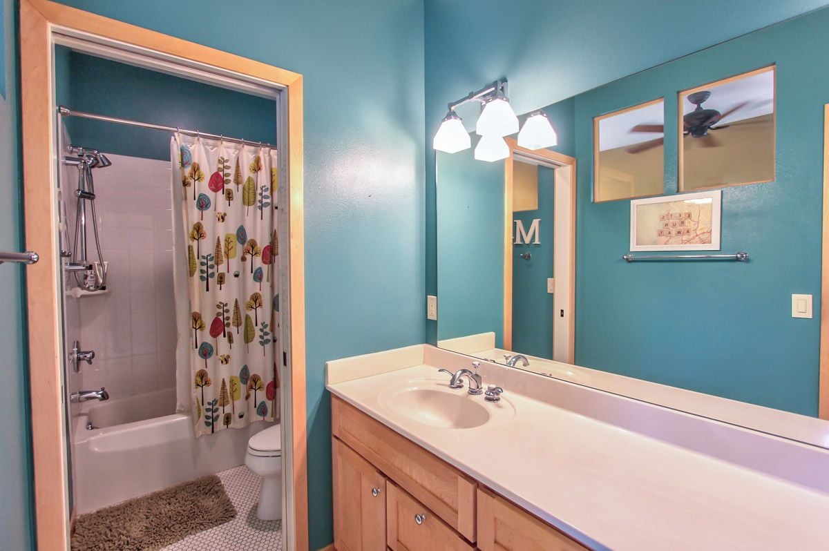 Bathroom with turquoise walls, a long wood vanity, and a tub and shower behind a patterned curtain.