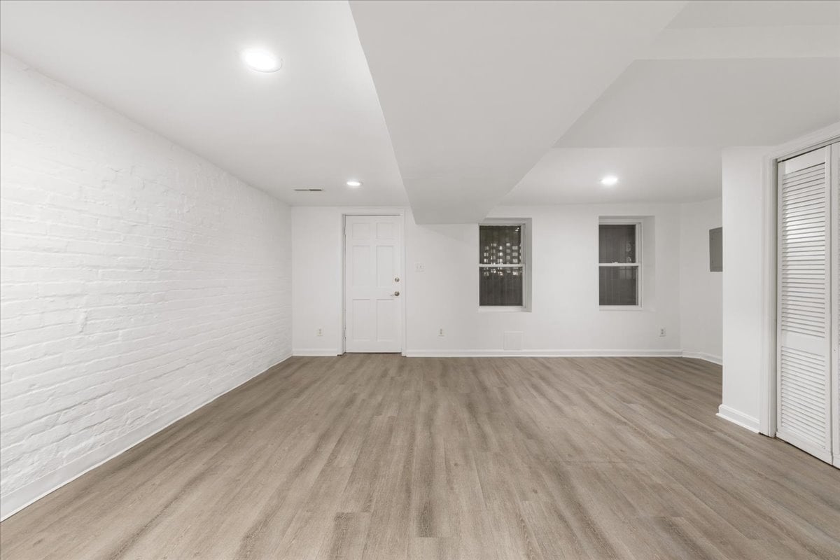 Empty room with wood-look floors, a white brick wall, two windows, and recessed lights.