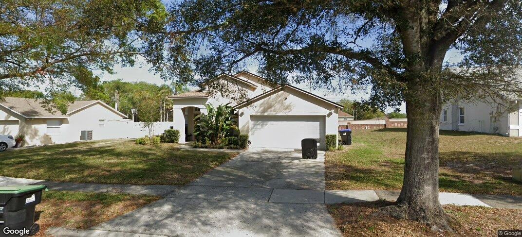 Single-story white house with an attached garage, driveway, and large shade tree in front.