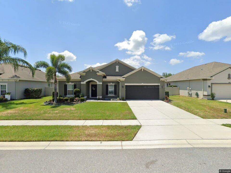 Gray single-story home with an attached garage, palm trees, and a broad concrete driveway.