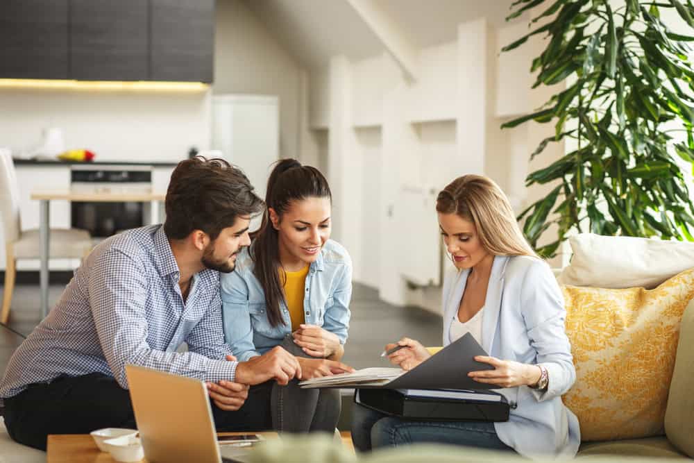 A real estate agent reviews paperwork with a couple in a bright living room.