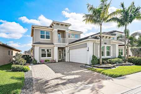Modern two-story home with a white garage, paved driveway, landscaped lawn, and palm trees.