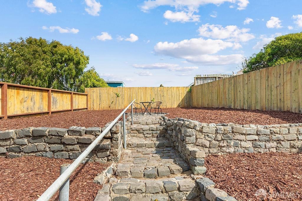 Fenced backyard with stone steps, a metal handrail, and a raised seating area.